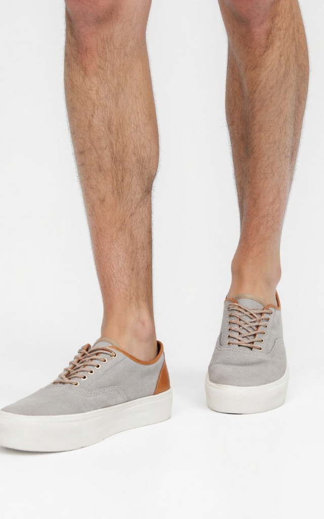 A male model wearing Canvas shoes with leather trims, against a white background, with a close   up of the feet